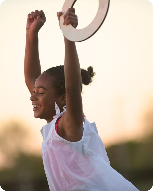 Girl playing outdoors with on playground rings overhead at golden hour